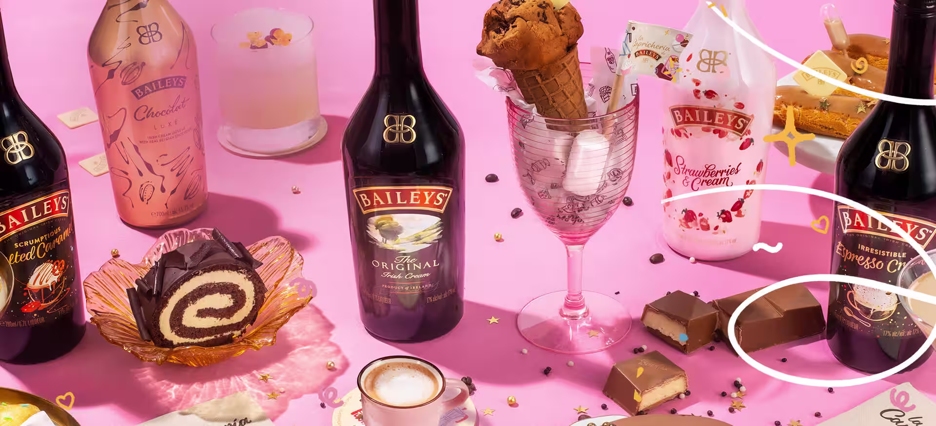 Various sweets and Baileys bottles on a pink table