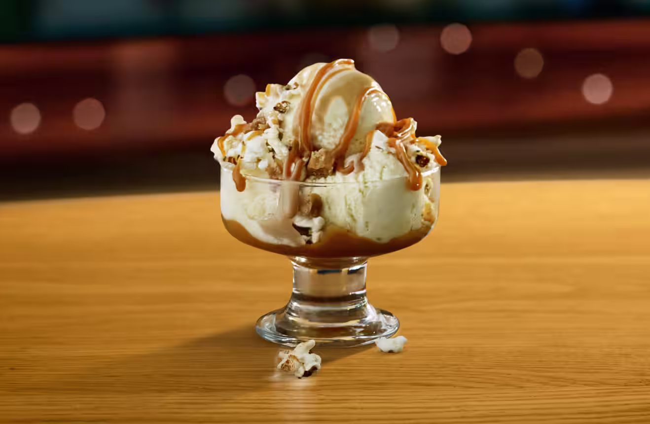 Creamy vanilla ice cream drizzled with golden caramel, topped with crunchy popcorn in a glass dessert dish—sweet, salty, and totally irresistible.